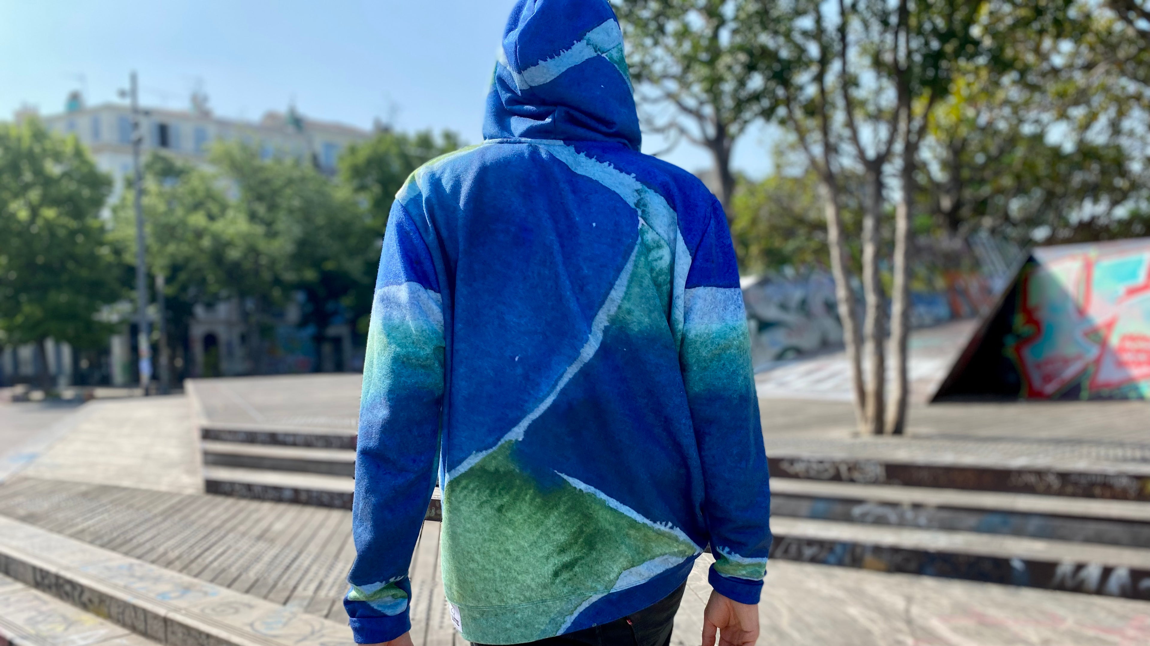Person wearing a blue and green gradient hoodie outdoors on a sunny day.